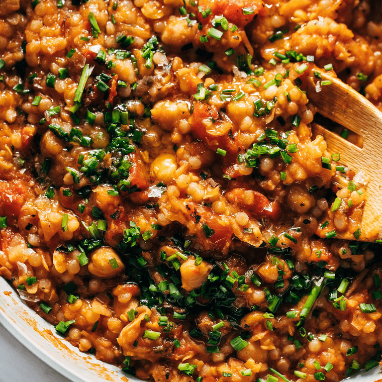 Pearl couscous in a skillet with tomatoes.