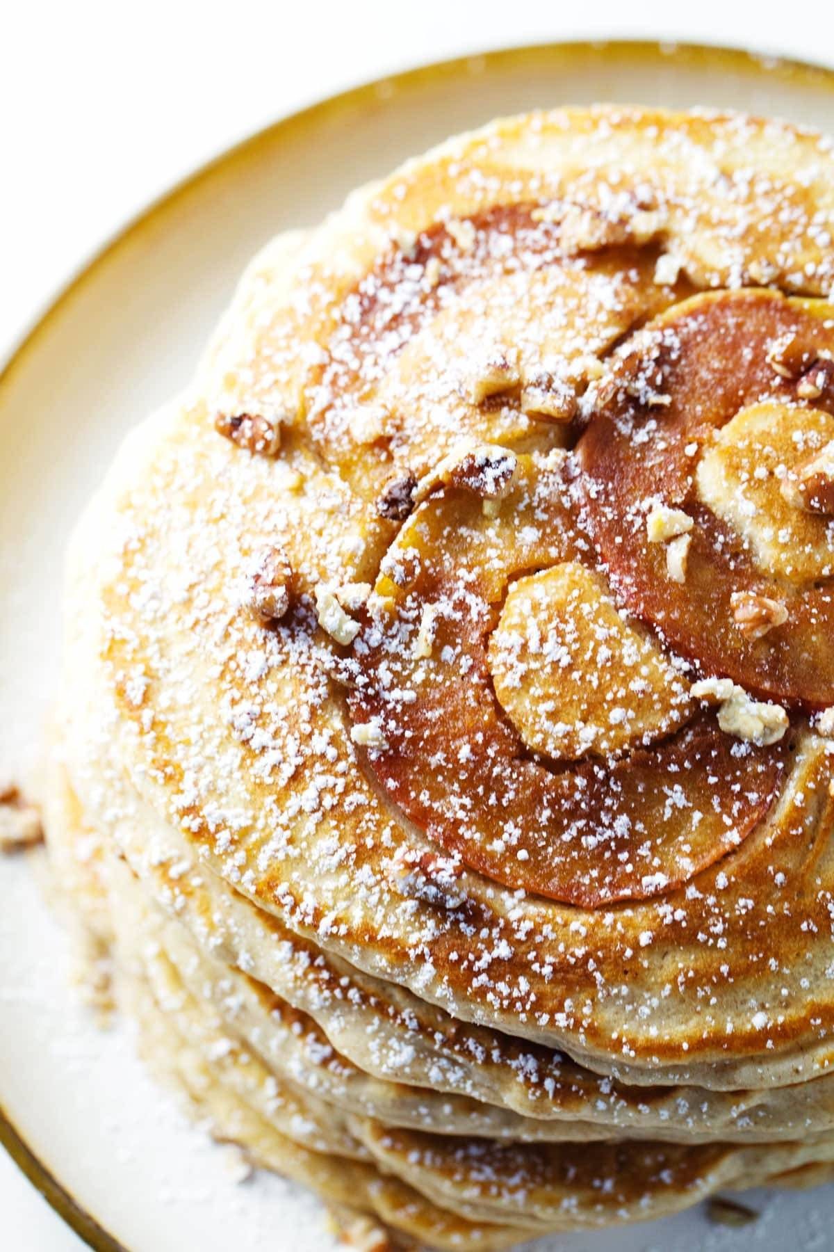 Apple pancakes stacked on a plate with powdered sugar.